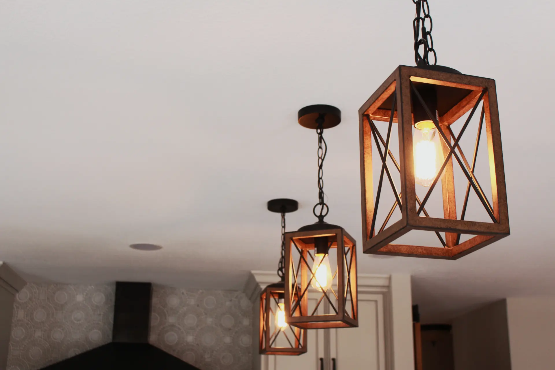 Three rustic pendant lights with metal frames hanging from a ceiling in a kitchen.