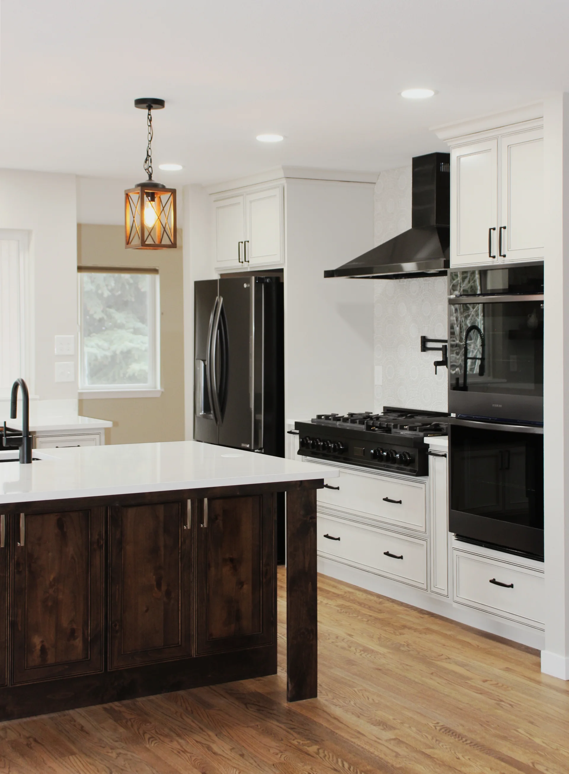 Modern kitchen with white cabinetry, dark wood island, black appliances, and hardwood floors.