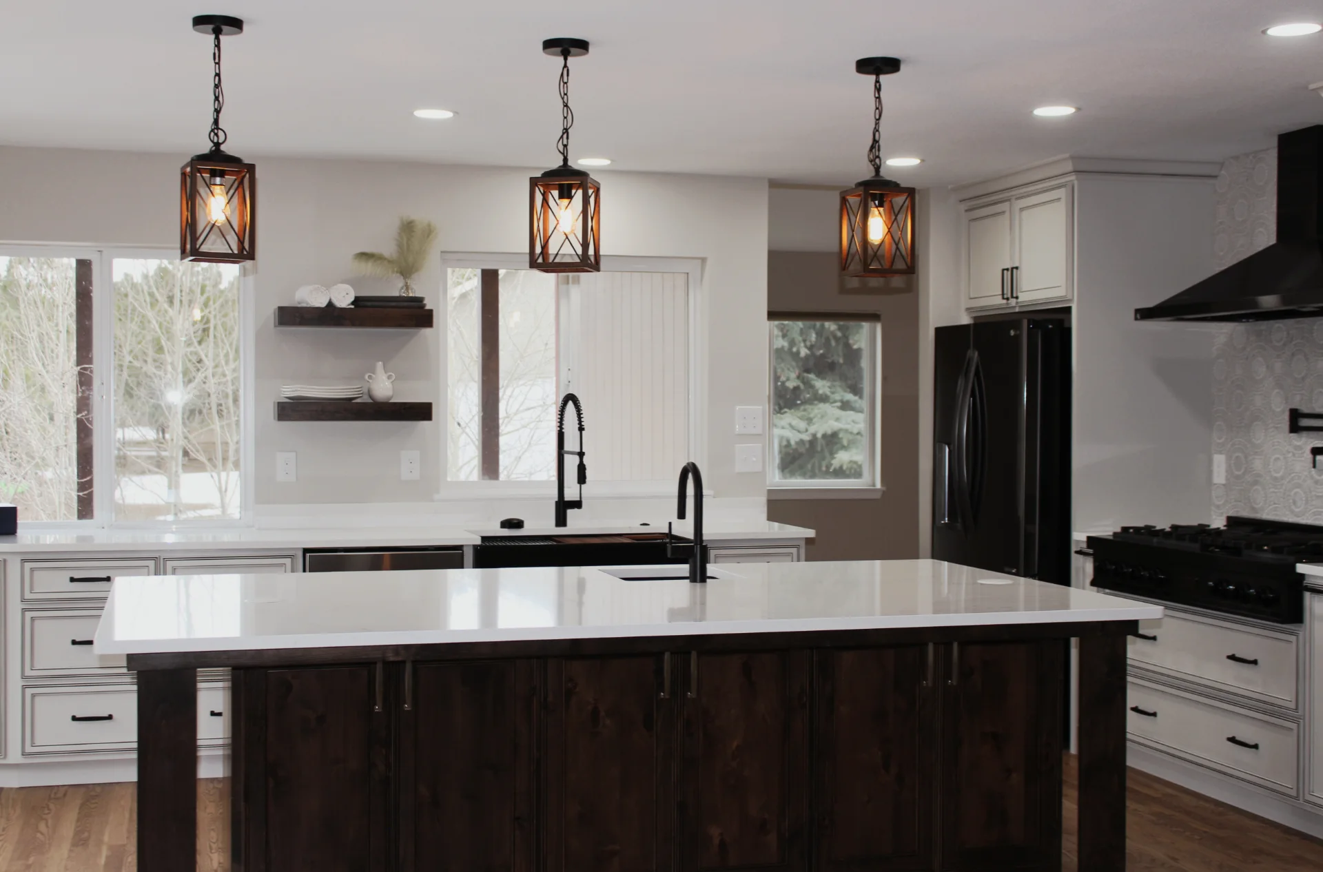 Modern kitchen with a large white marble island, dark wood base, black fixtures, pendant lights, and white cabinetry.