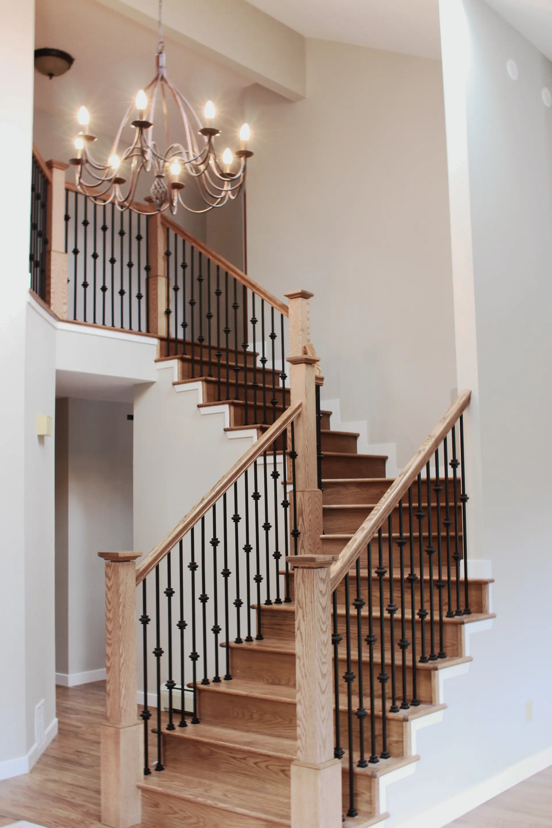 Modern wooden staircase with black metal balusters and a decorative chandelier hanging above.