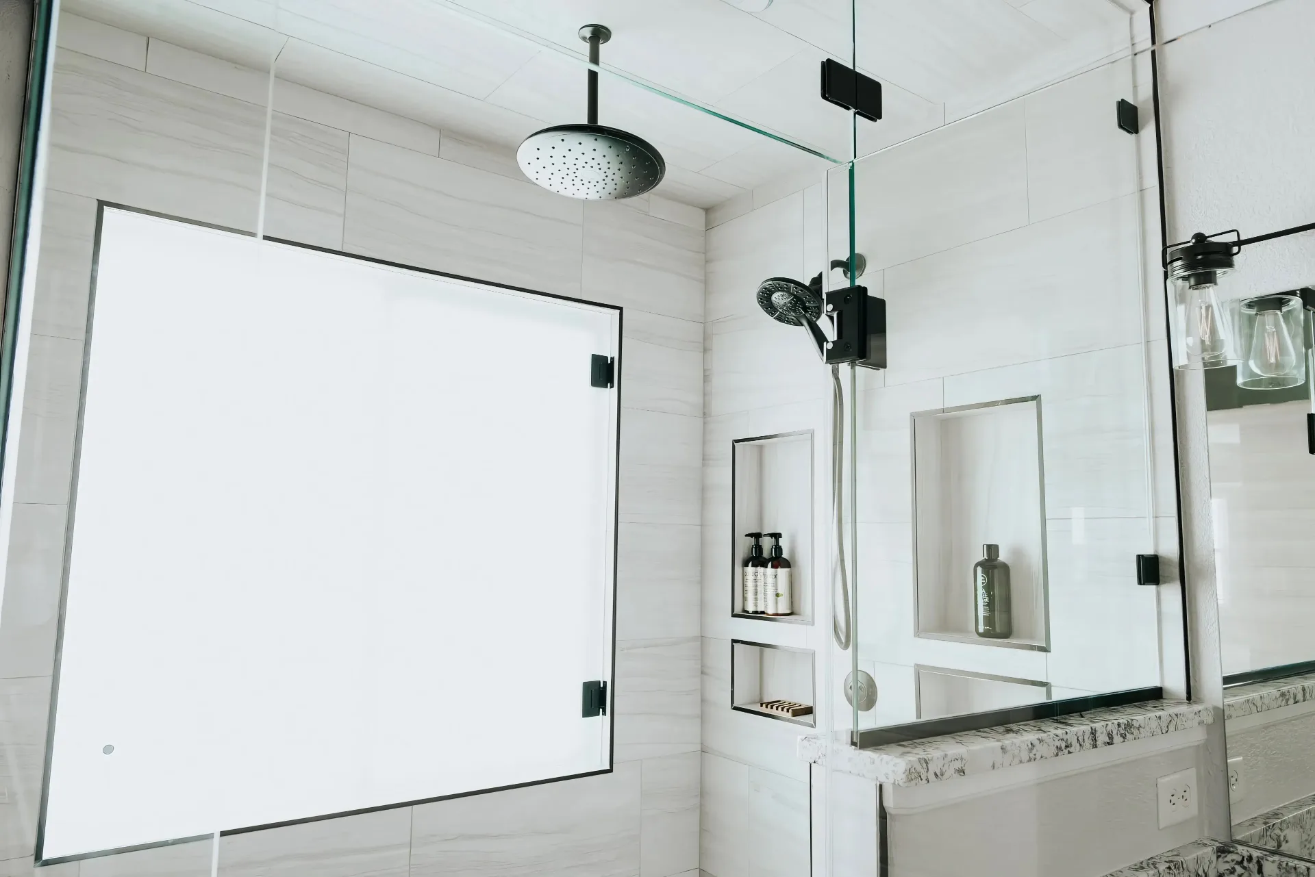 Modern bathroom shower area with large square overhead showerhead, handheld shower, built-in shelves, and frosted glass window.
