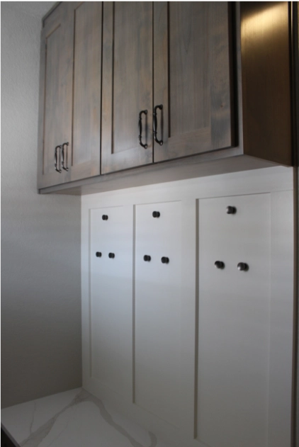 Custom mudroom cabinets with dark wood upper storage and white panelled lower wall with black coat hooks.