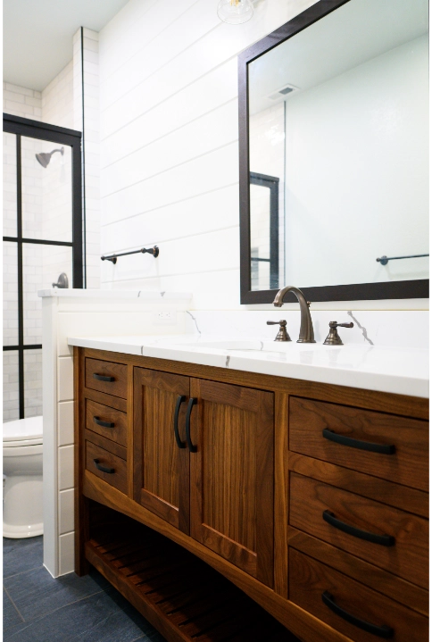 Modern bathroom vanity with dark wood cabinetry, white countertop, and a large framed mirror above.