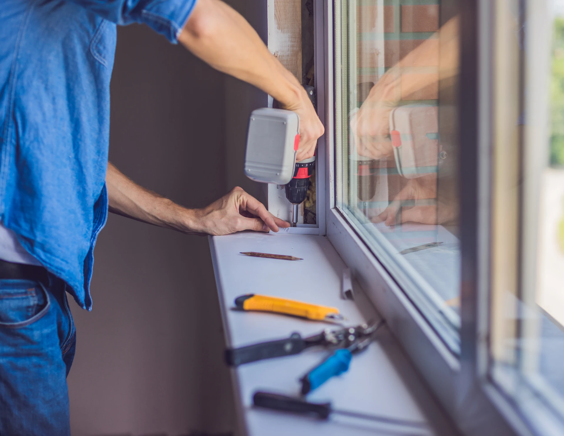 Person using a cordless drill to install a window frame inside a home.