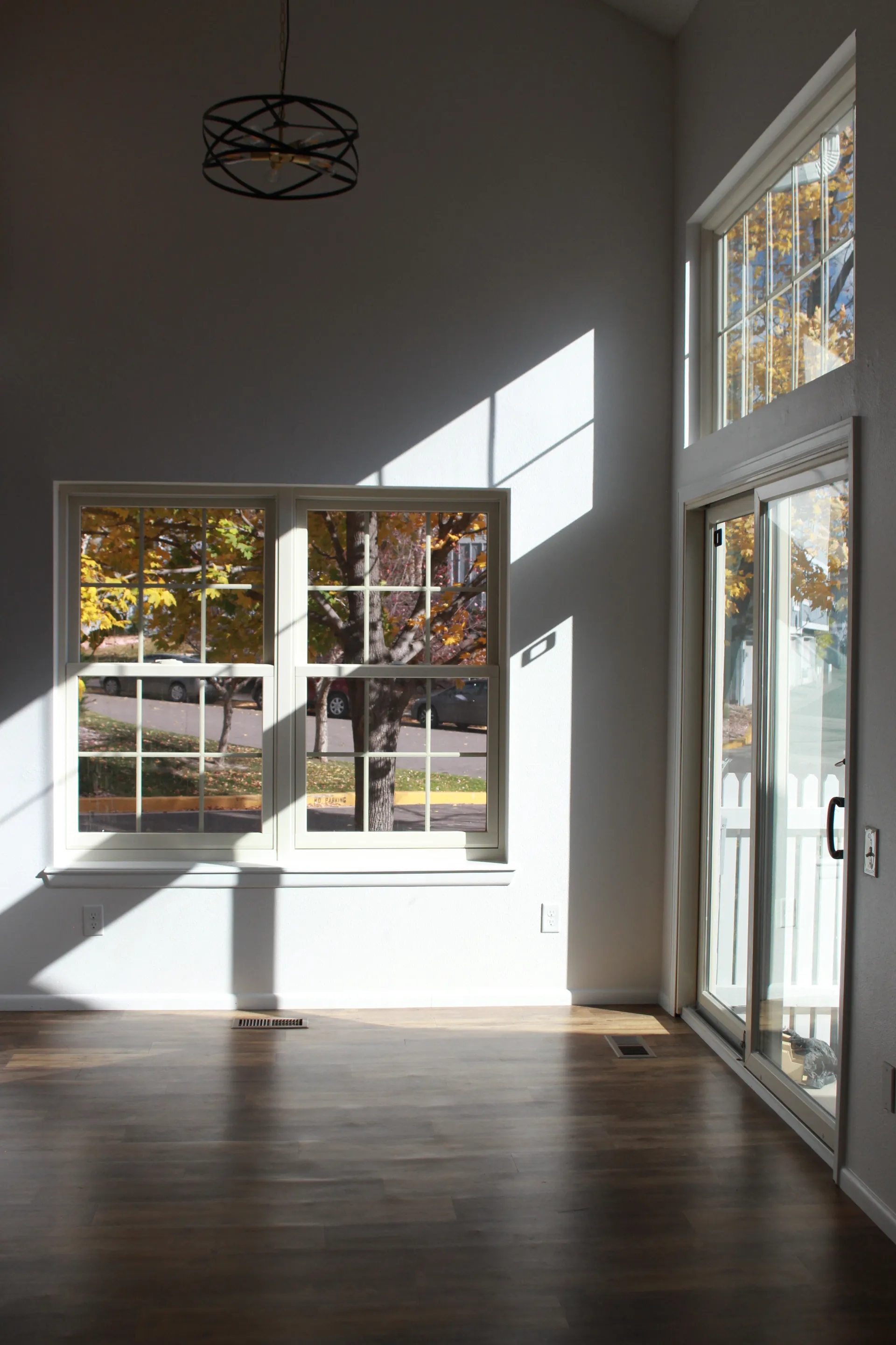 Empty room with newly installed white framed windows and sliding glass door letting in autumn sunlight.