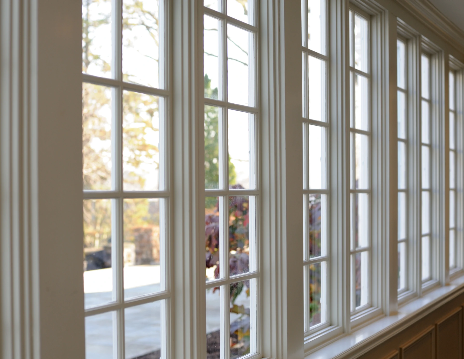 Interior view of large white-framed windows showing blurred autumn foliage outside.
