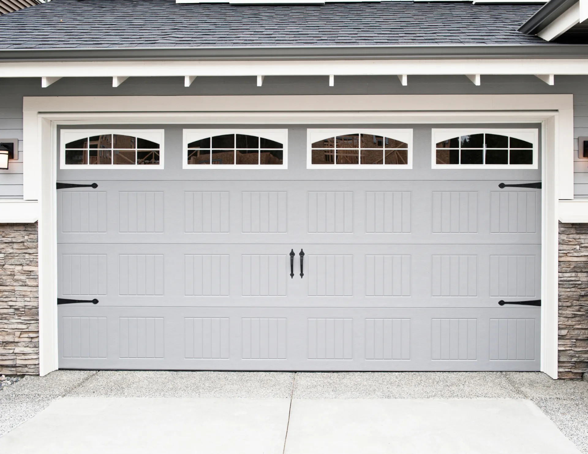 Closed light gray sectional garage door with four arched windows at the top and black decorative handles.