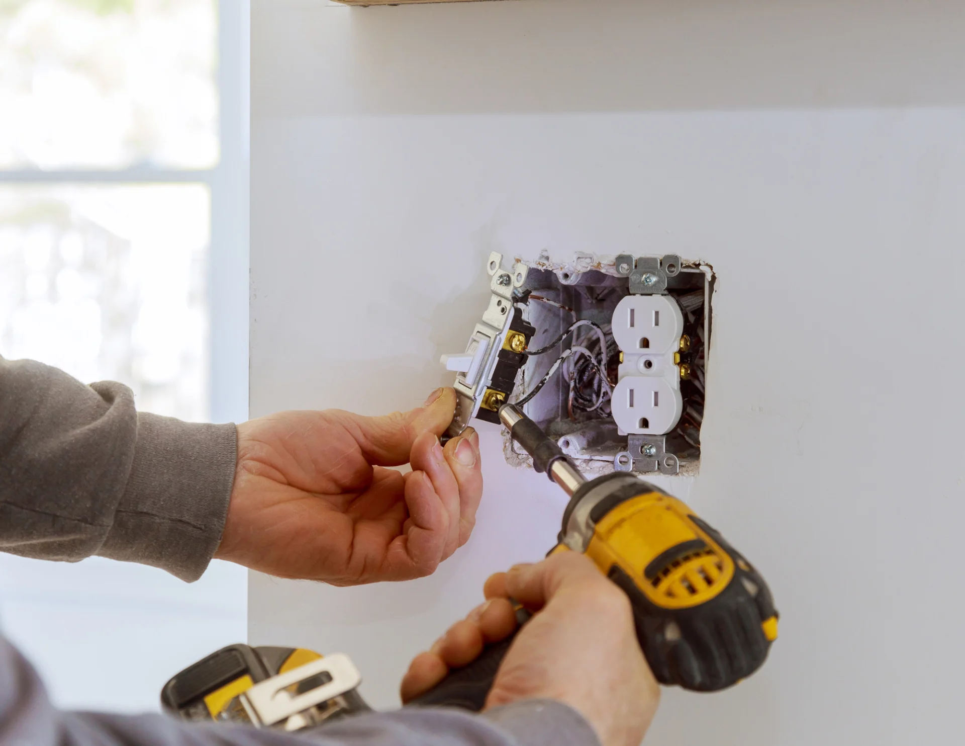 Electrician installing a light switch with a screwdriver near a wall outlet box.