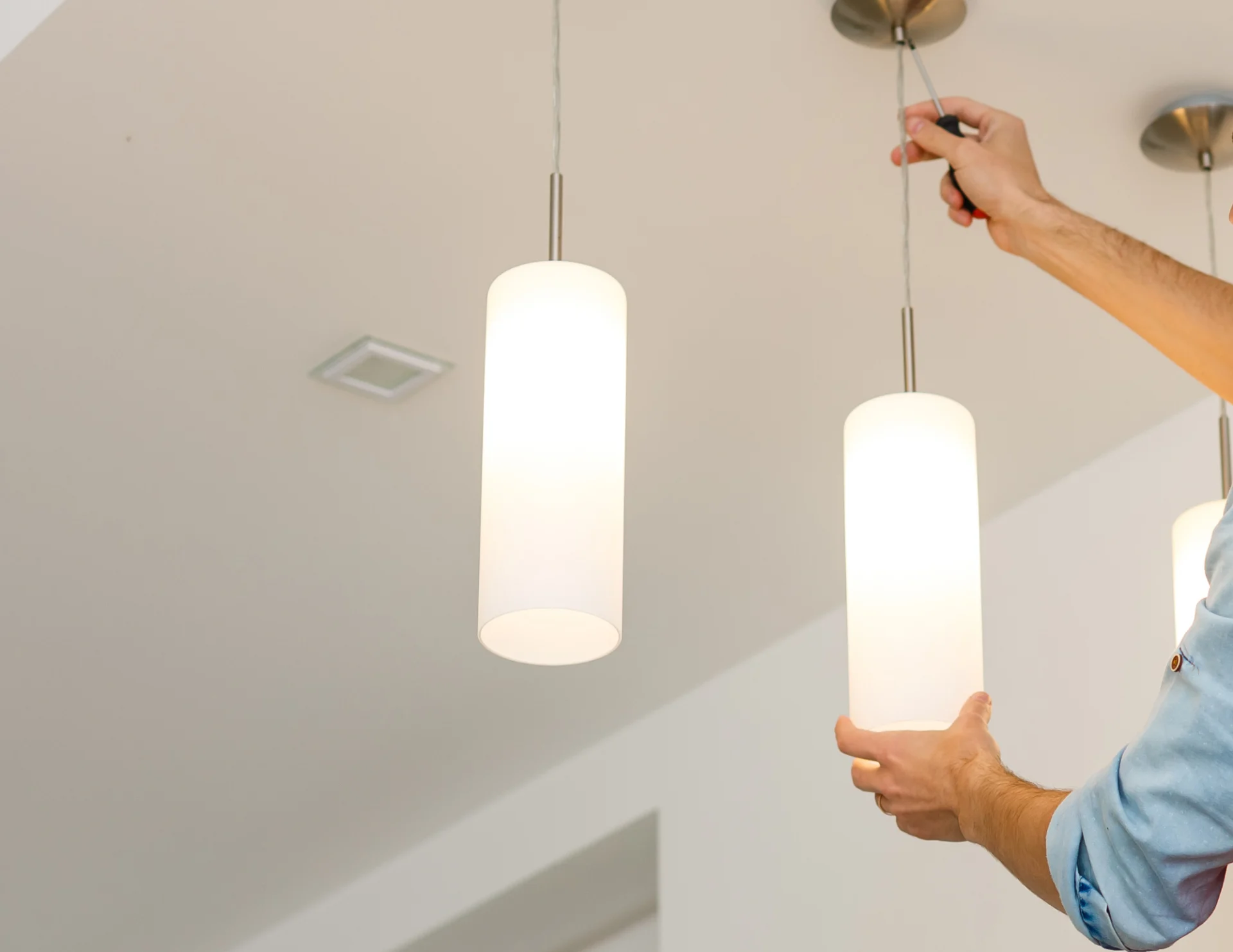 Person installing or adjusting a modern cylindrical pendant light fixture on a ceiling.