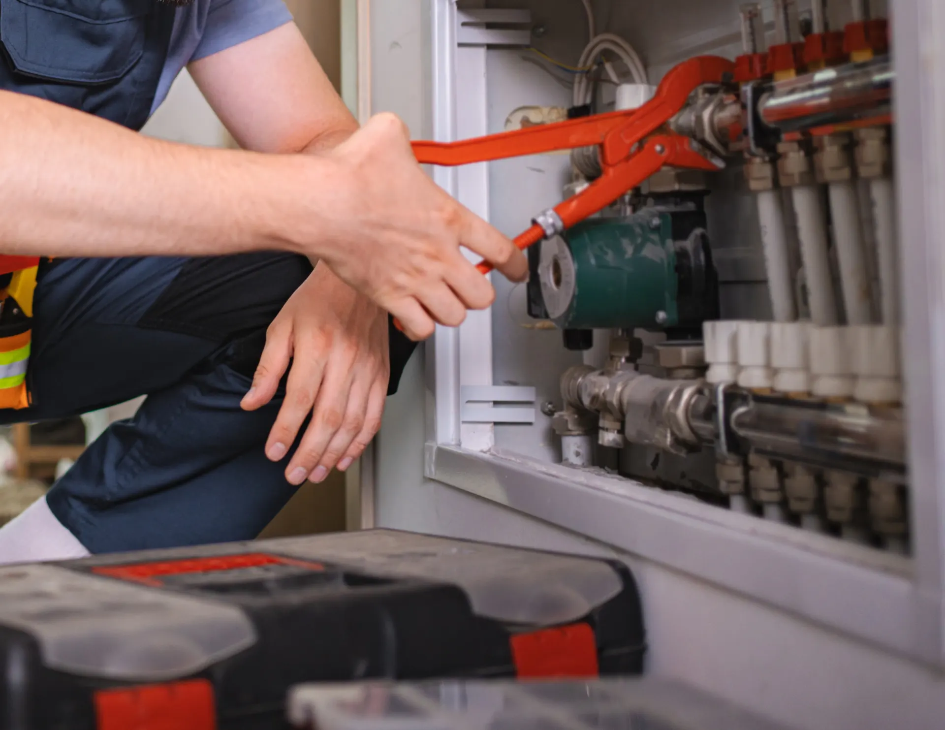 Technician using a red pipe wrench to adjust valves in a heating system panel.