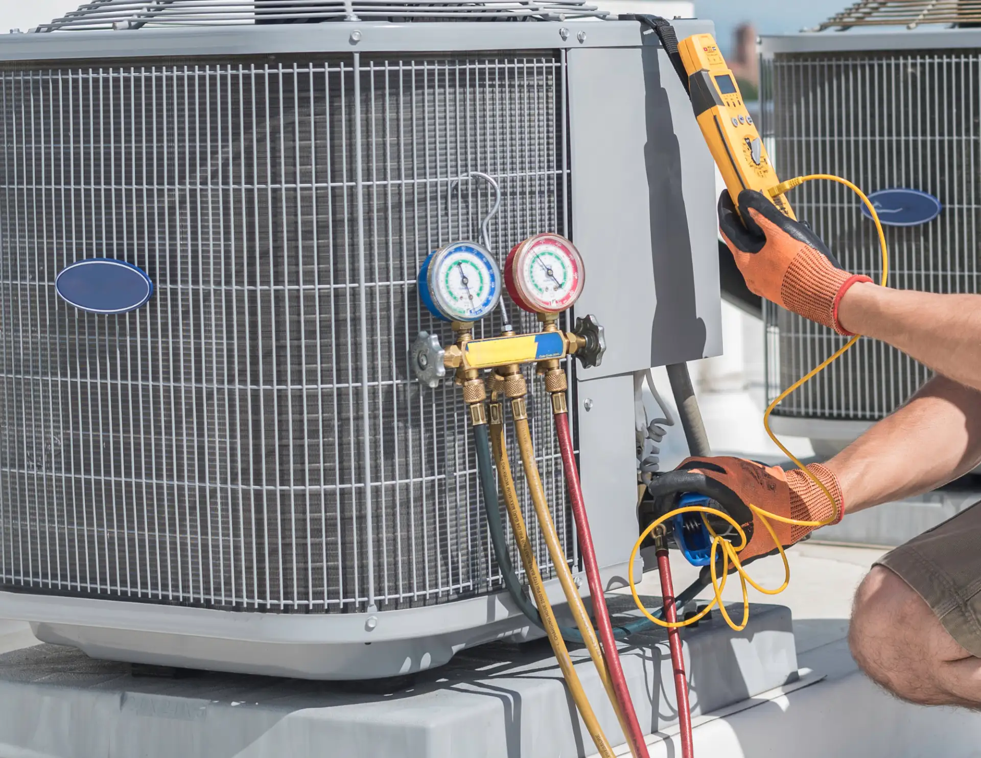 Technician wearing orange gloves using diagnostic tools to check an air conditioning unit's refrigerant pressure.
