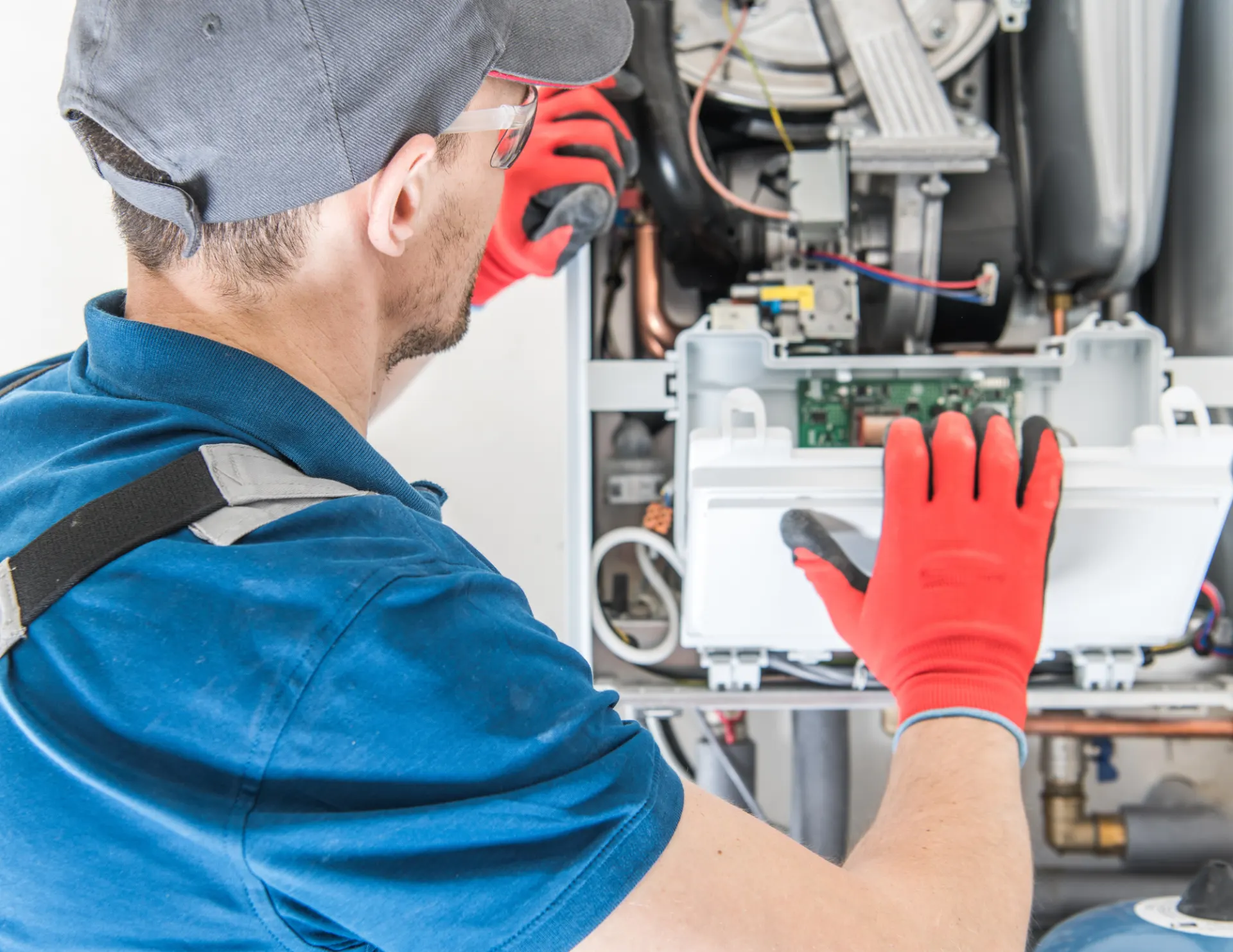 Technician in red gloves and blue shirt inspecting the inside of a HVAC unit.