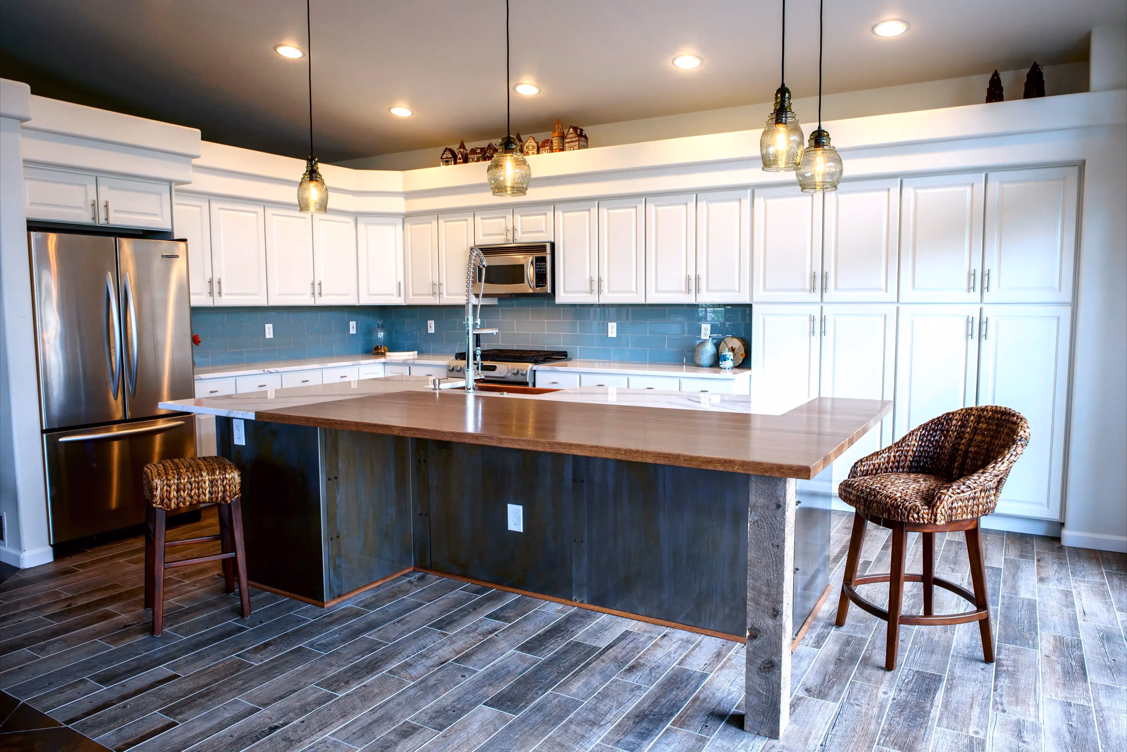 Modern kitchen with white cabinets, stainless steel appliances, a wooden island countertop, blue subway tile backsplash, and two wicker stools.