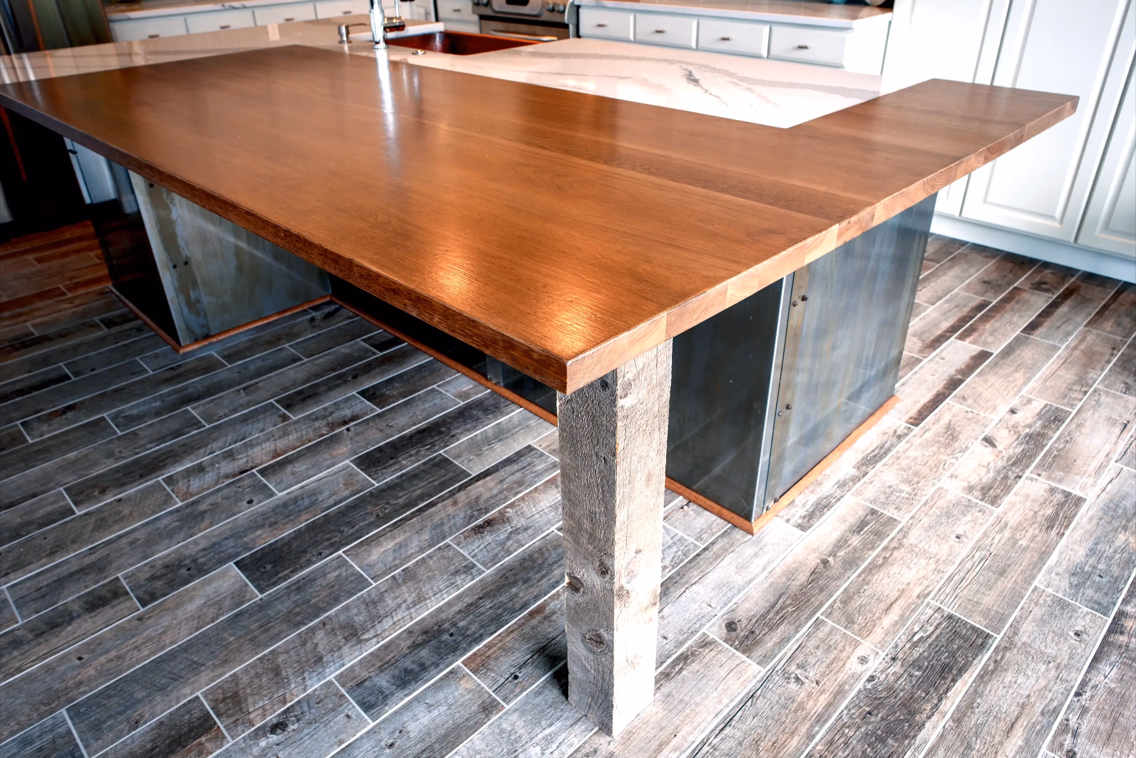 Modern kitchen island with a polished wooden countertop, metal sides, and a wooden support leg on wood-look tiled floor.