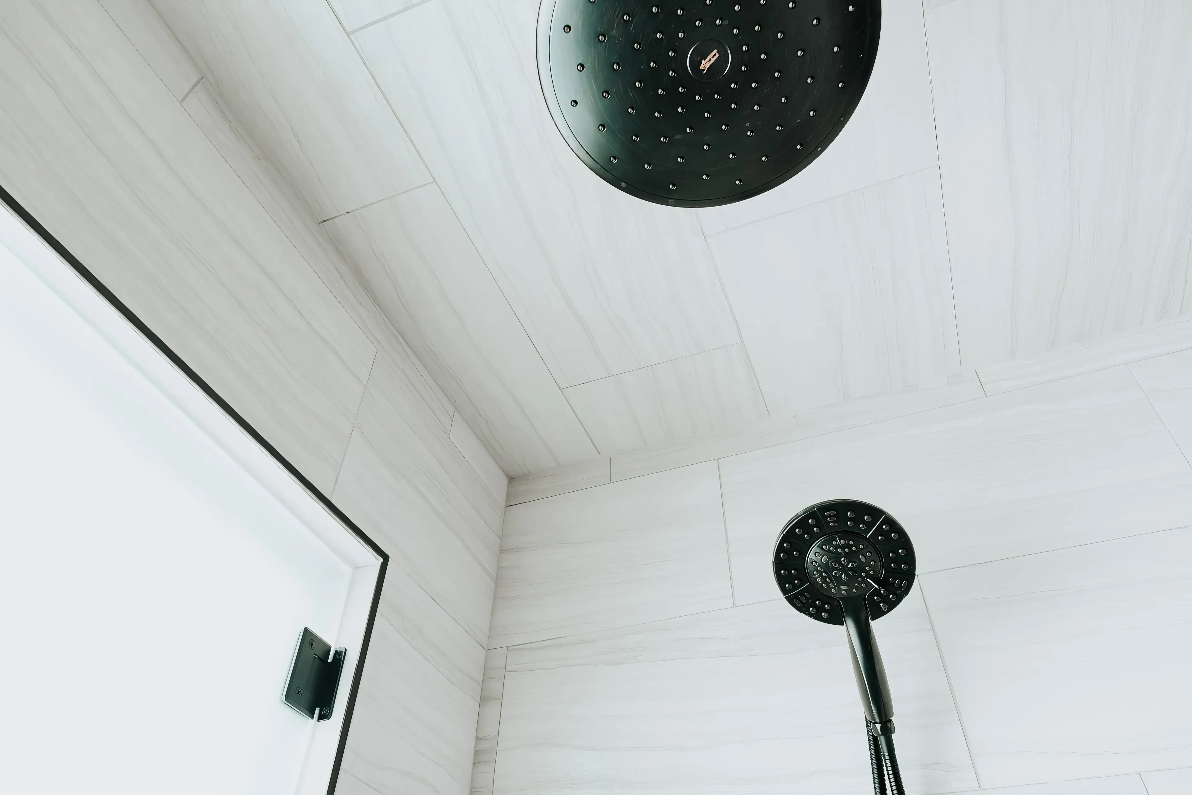 Modern bathroom corner with white marble tiles and black rain showerhead and handheld shower.