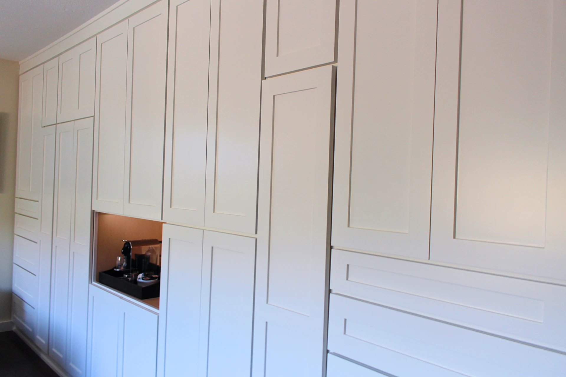 Wall of white built-in cabinets with a recessed coffee station holding a coffee maker and accessories.