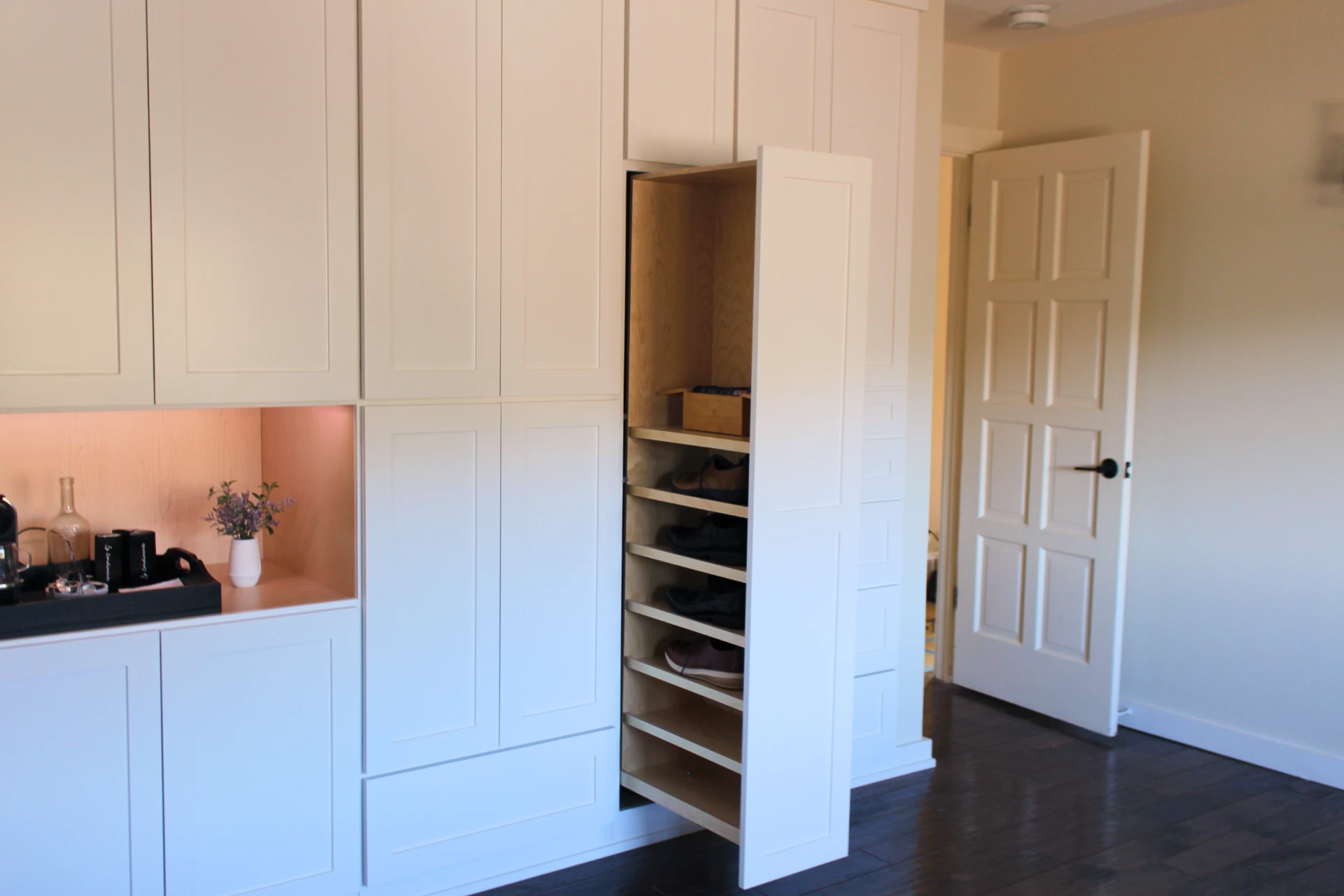 Modern white built-in cabinetry with an open pull-out shoe rack and dark wood flooring.