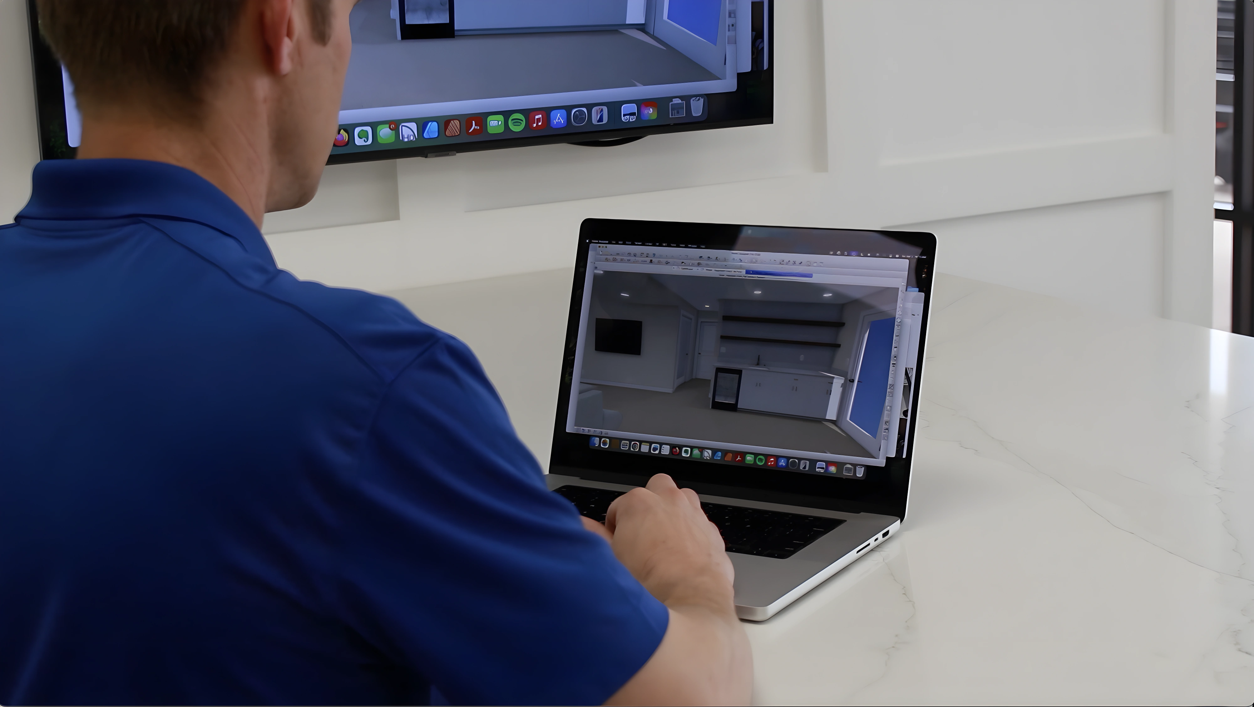 Person in blue shirt designing a modern wet bar on a laptop at a white marble table.