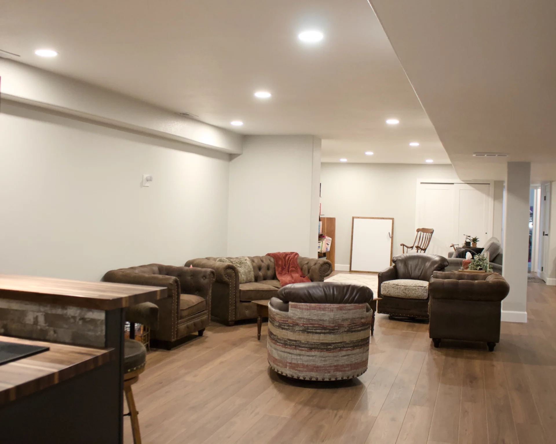 Modern basement seating area with brown leather chairs, couch, wood flooring, and recessed ceiling lights.