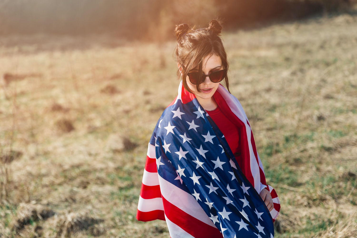A woman wearing sunglasses with an American flag draped around herself.