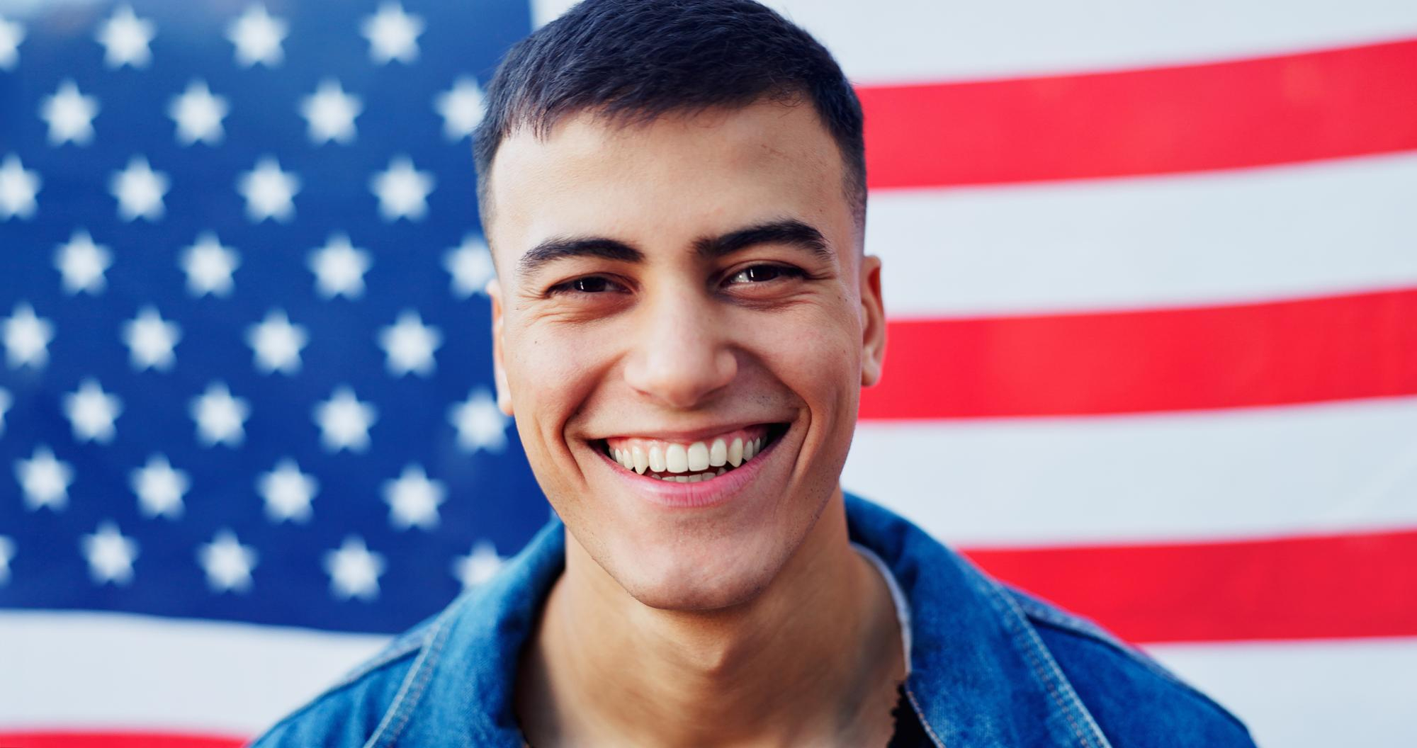 A man smiling in front of an American flag.