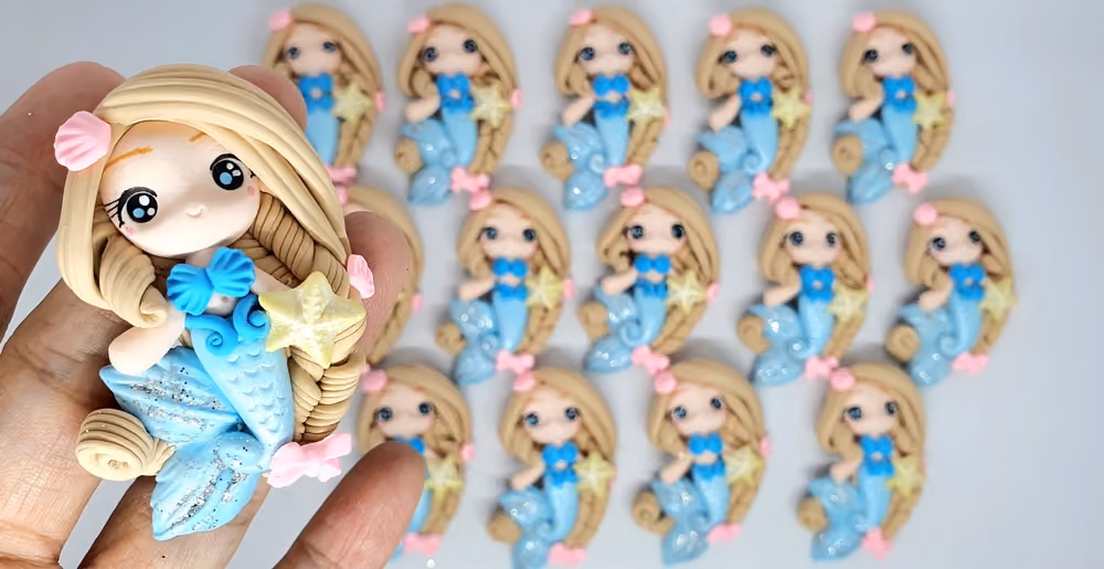 Hand holding a small blue mermaid figurine with blonde hair and starfish, with more mermaid figurines blurred behind.