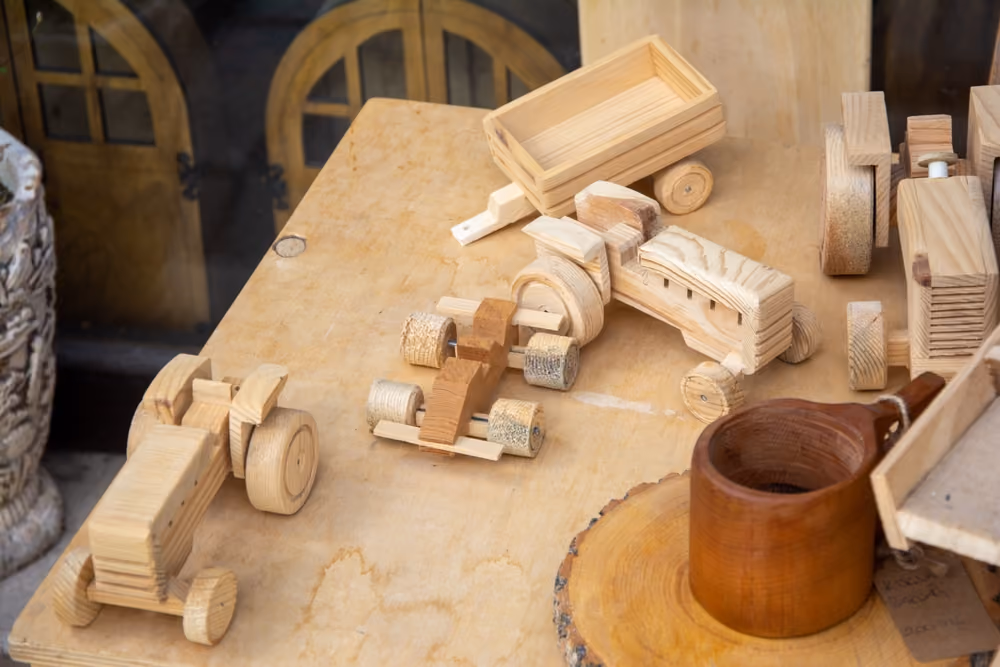 Wooden handmade toy vehicles and a cup displayed on a light wood table.