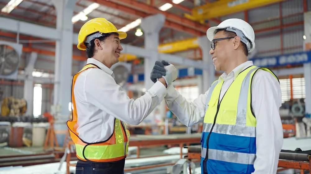 Two workers greeting each other on a factory floor.