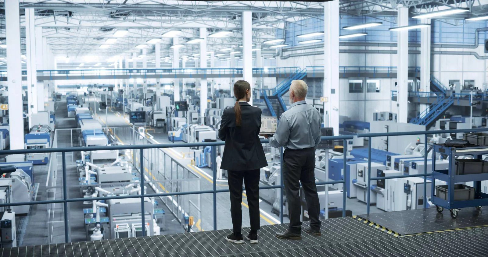 Two people reviewing production facilities from a factory walkway.