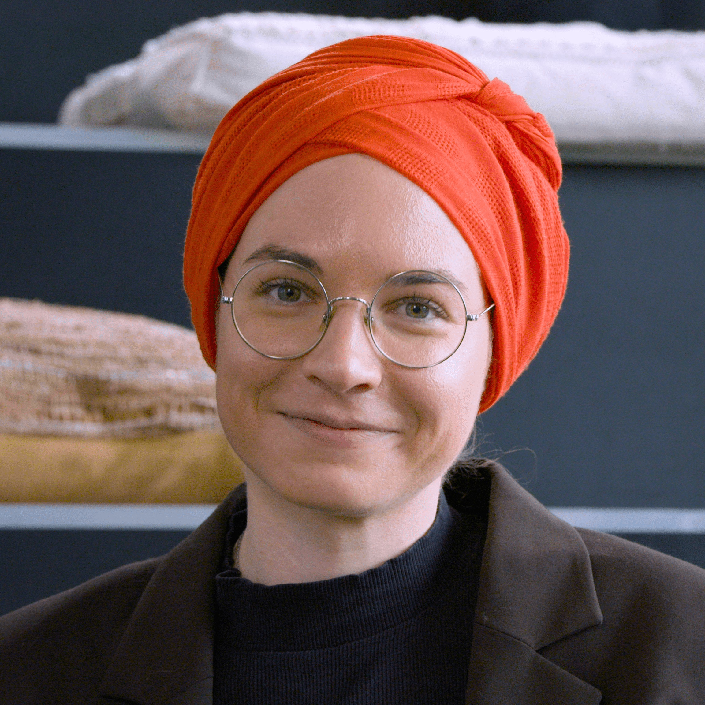 Picture of a smiling lady wearing round glasses and an orange head-covering.