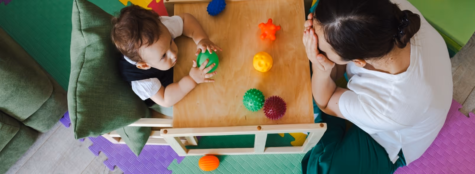 A baby playing with a ball on a wooden table.