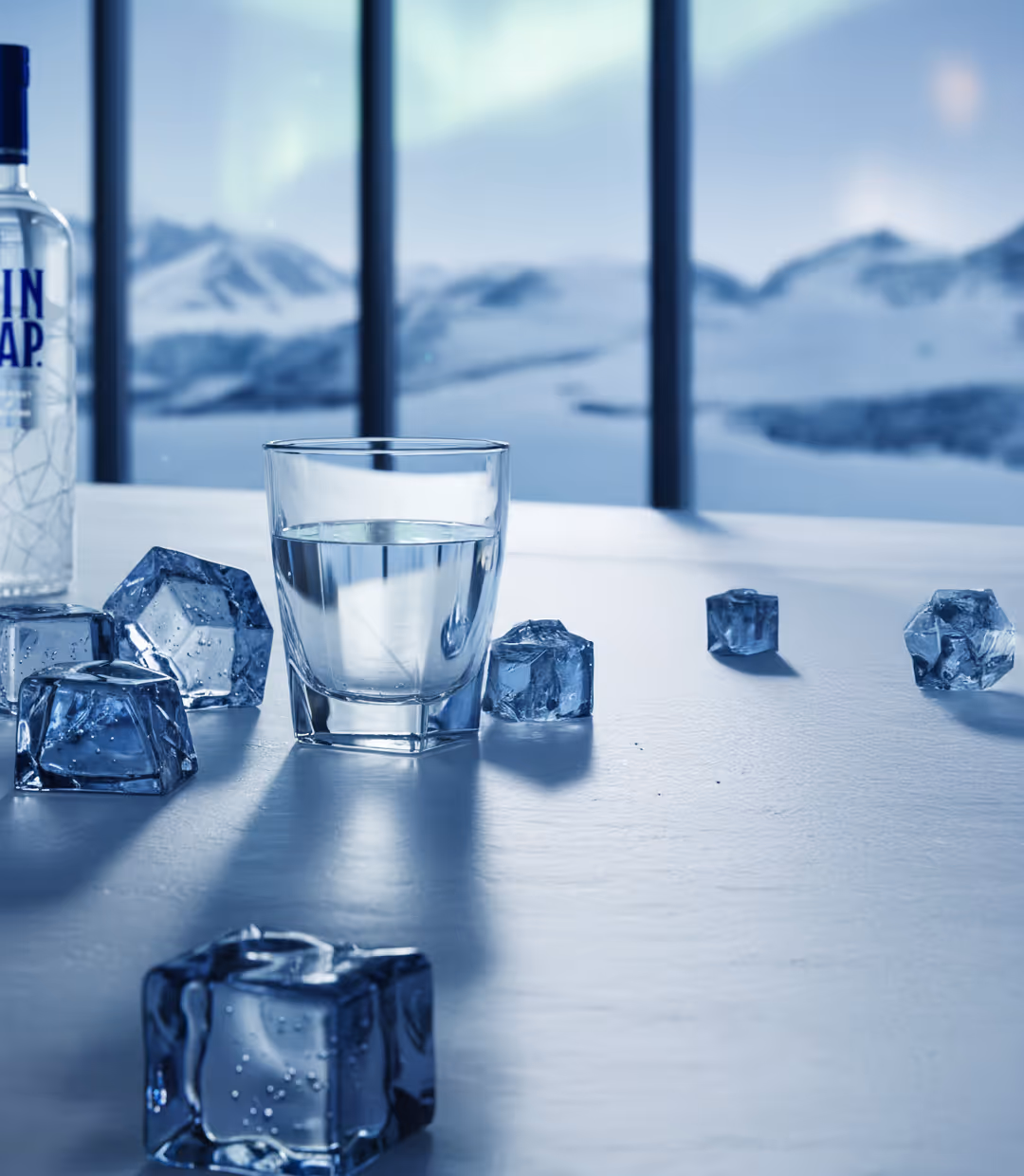 Glass of clear liquid with scattered ice cubes on a reflective surface against a snowy mountain backdrop.