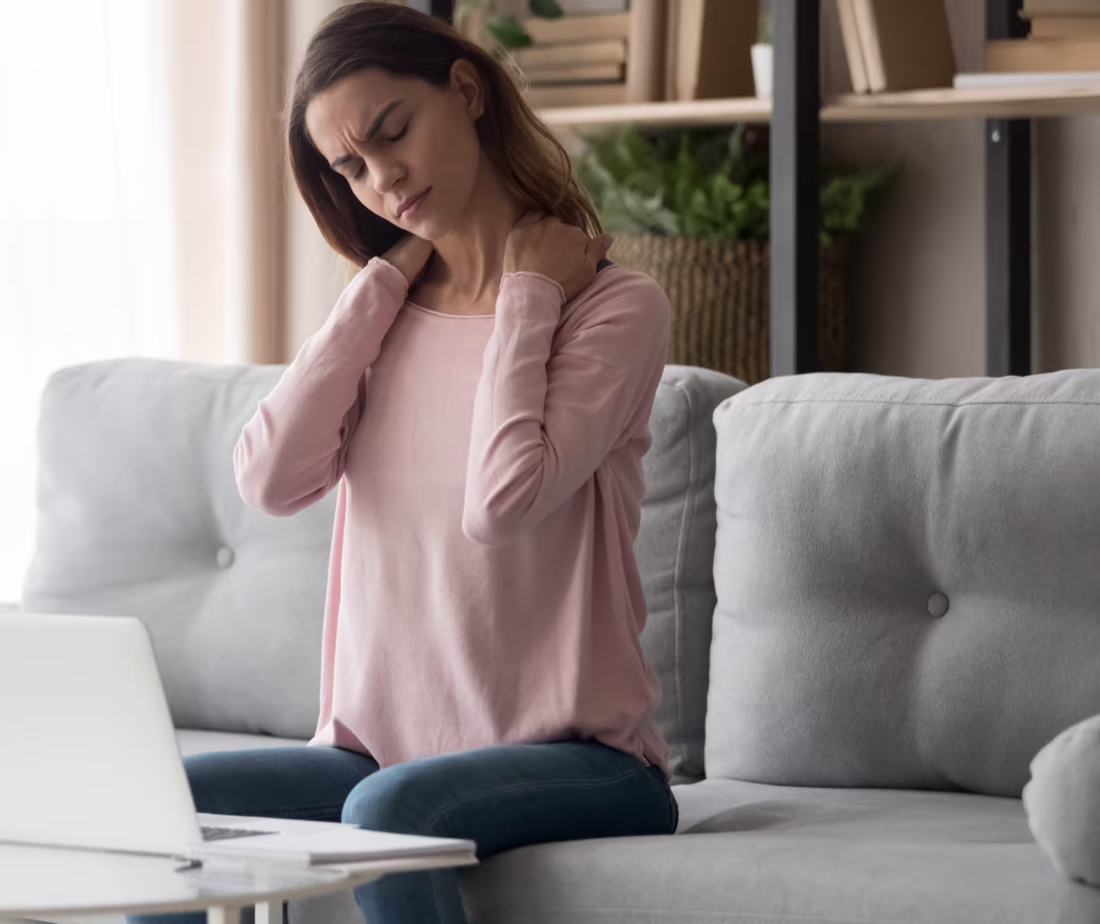 Woman sitting on a couch holding her neck in pain