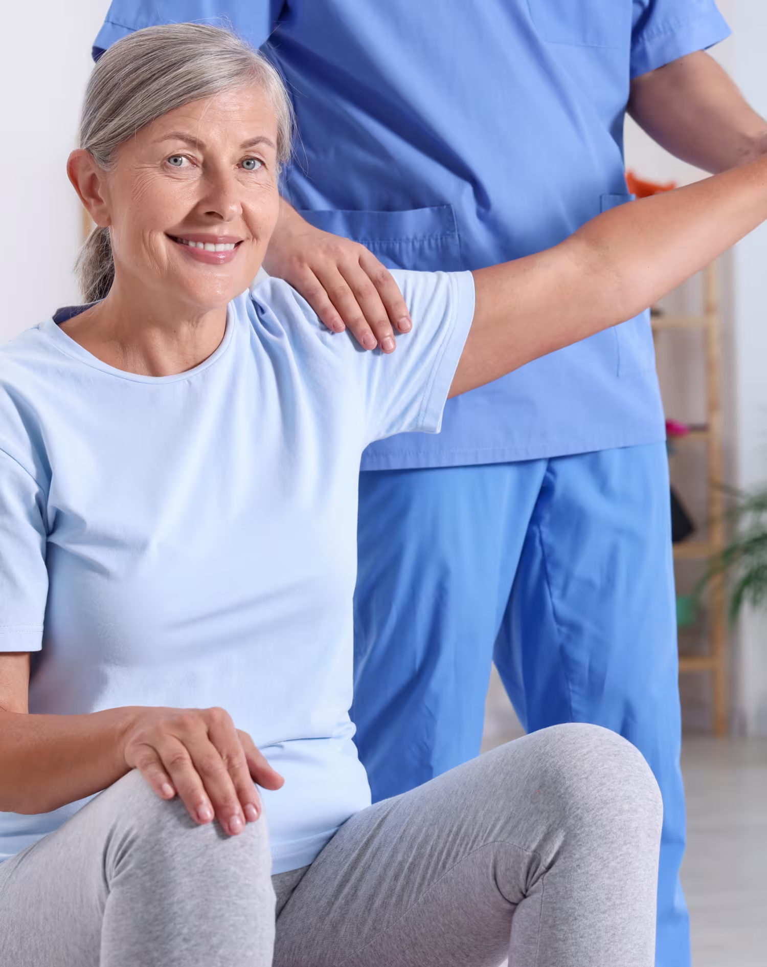 Smiling older woman doing shoulder exercise with assistance from a healthcare professional