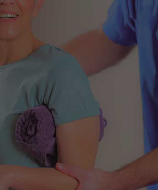 Physical therapist assisting a smiling woman with a shoulder exercise using a rolled towel under her arm