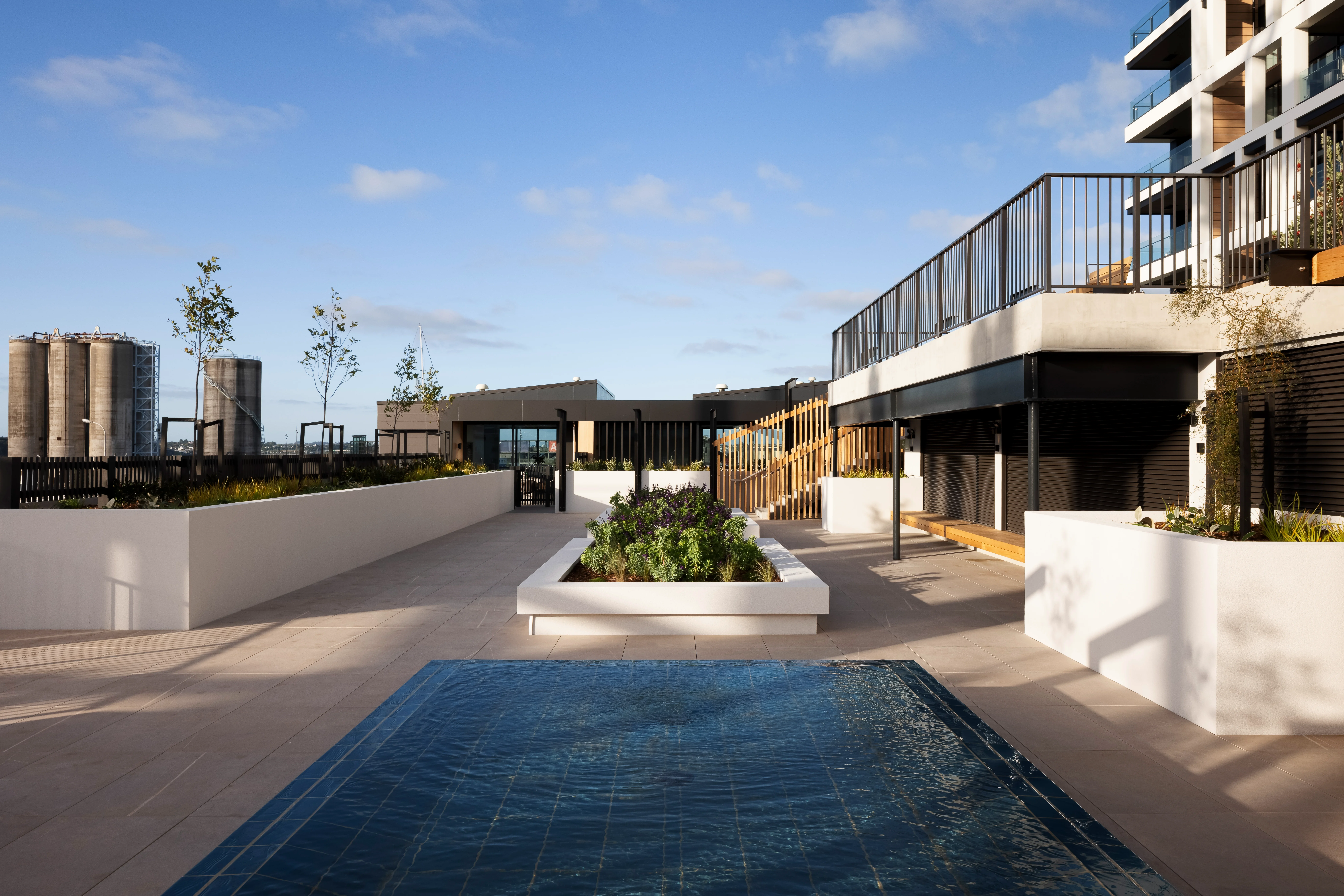 Rooftop terrace with a pool, timber stairs, and planter boxes, with black balustrades along the stairway and upper balcony