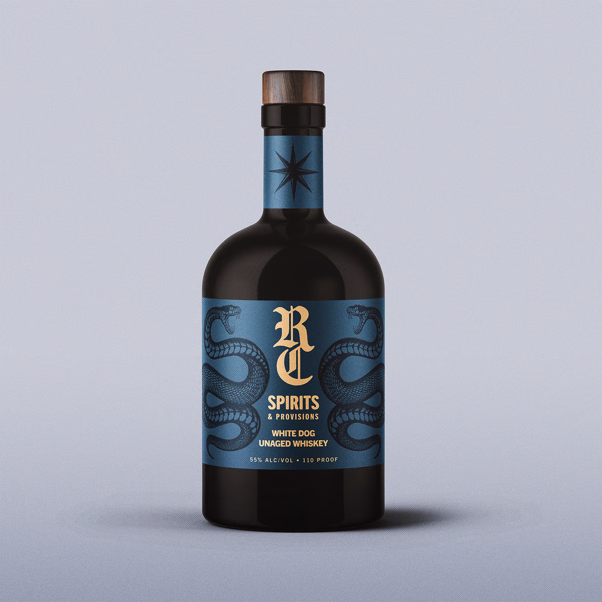 Dark bottle with a wide neck and wooden cap featuring a blue label with two black snakes and gold text reading RC Spirits & Provisions White Dog Unaged Whiskey 55% Alc/Vol 110 Proof.