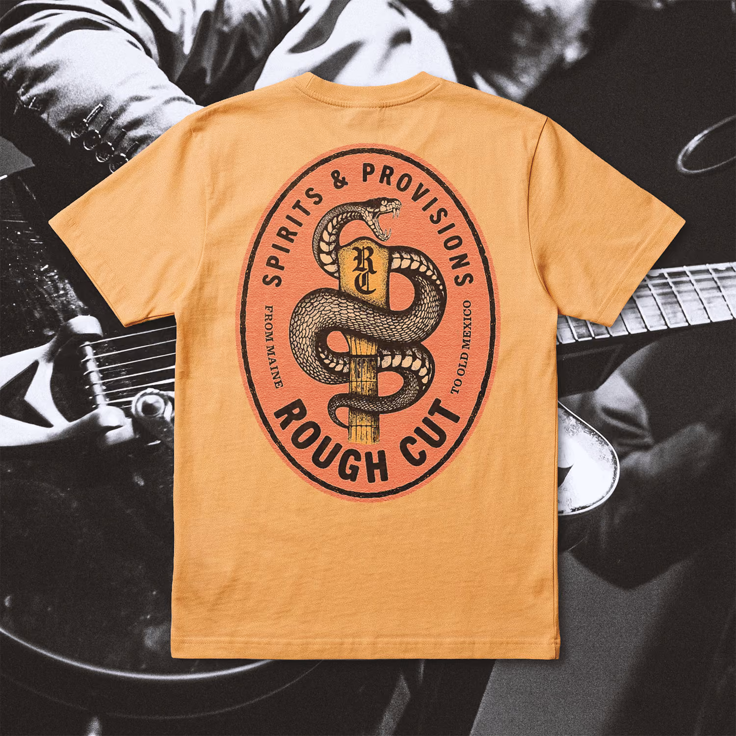 Light brown t-shirt with a large oval graphic on the back featuring a coiled snake wrapped around a wooden stake, surrounded by the text 'Spirits & Provisions Rough Cut' and smaller text 'From Maine to Old Mexico'.