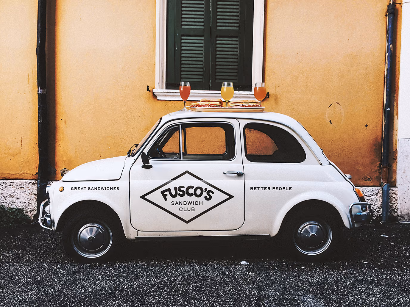 White Fiat car with a diamond logo on the side in front of a stucco building