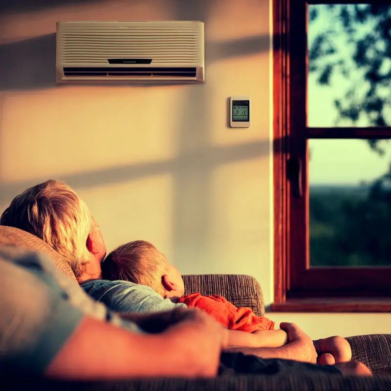 Grandparent and child relaxing under a ductless mini split AC unit in a cozy home setting during sunset.