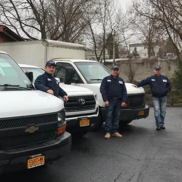 Certified Yukos Mechanical HVAC technicians standing beside company service vans in New York.