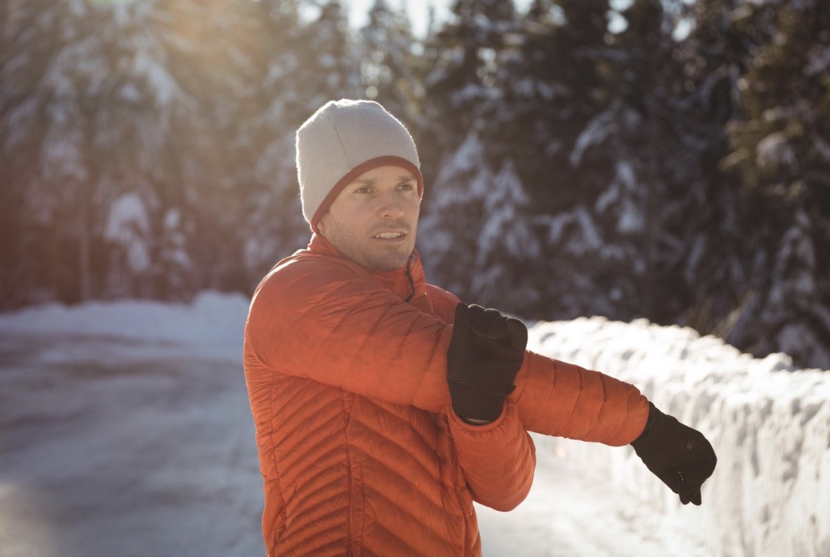 Mann wärmt sich im Winter mit Armdehnung im Freien auf, um sich aufs Skifahren vorzubereiten.