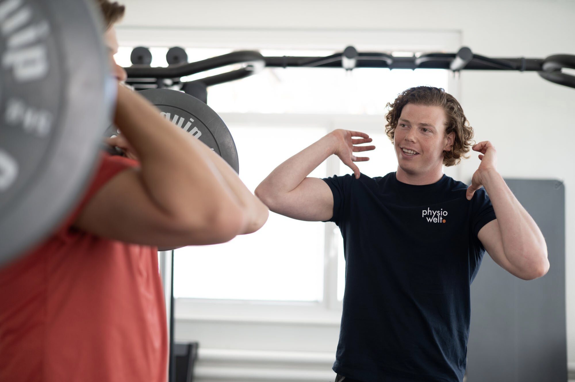 Physiotherapeut von PhysioWelt unterstützt einen Patienten bei funktionellem Training im Fitnessbereich zur Stabilisation der Schulter.