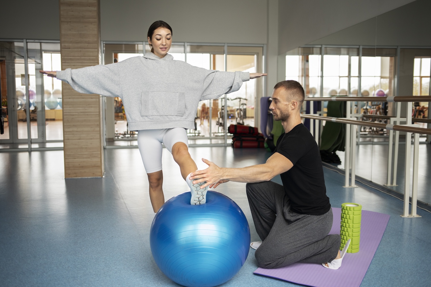 Physiotherapeut begleitet eine Patientin beim propriozeptiven Gleichgewichtstraining auf einem Gymnastikball.