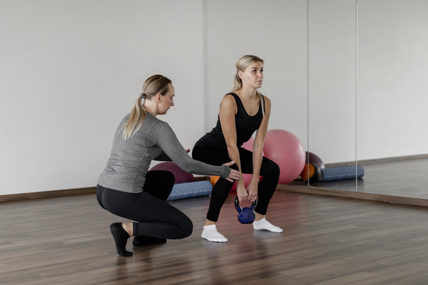 A physiotherapist guiding a woman through a kettlebell squat to build leg strength during rehabilitation.