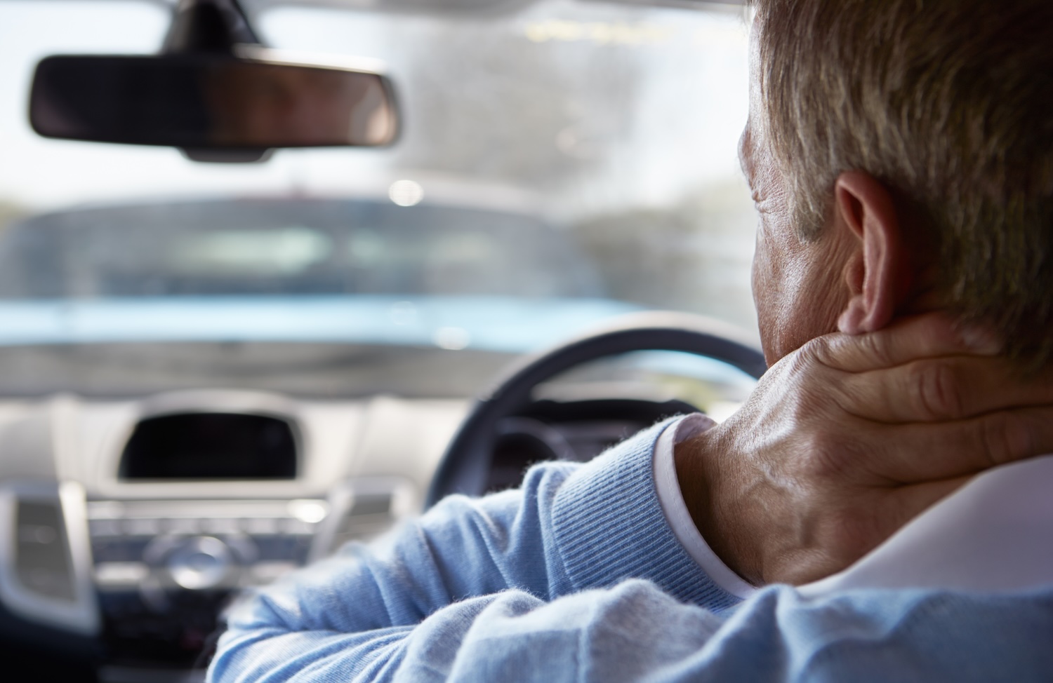Mann sitzt im Auto und hält sich nach einem Unfall den schmerzenden Nacken.