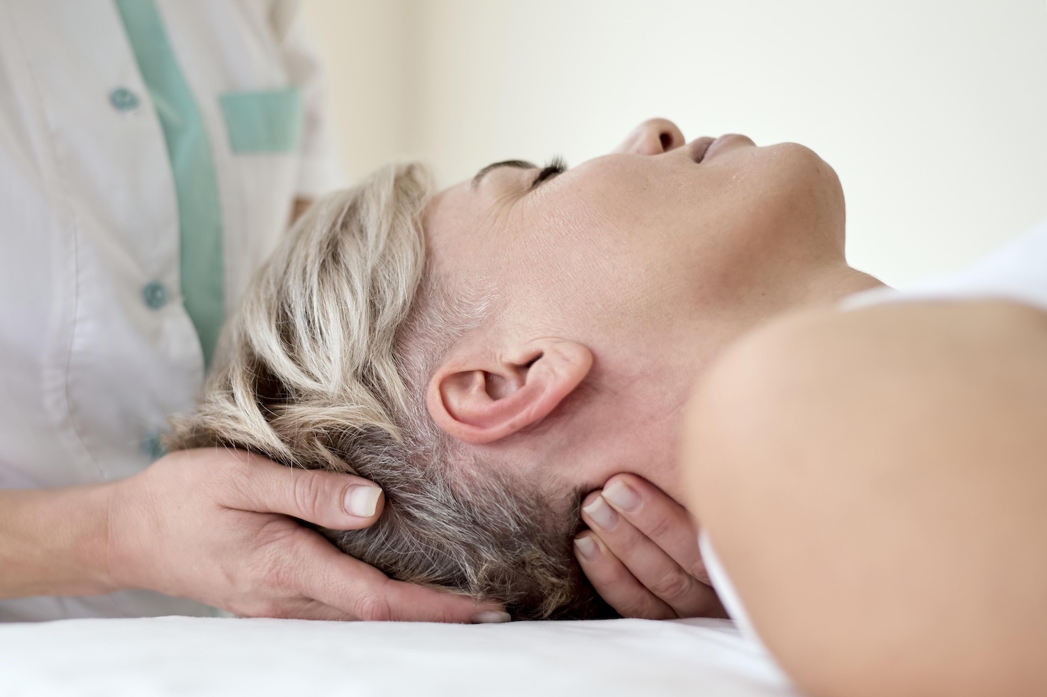 Physiotherapeutin mobilisiert sanft die Halswirbelsäule einer liegenden Patientin nach einem Schleudertrauma.