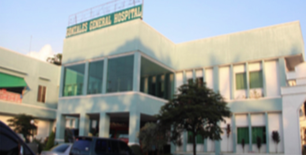 Two-story white medical building with green signage reading 'Gonzales General Hospital' on the upper facade, featuring large windows and a tree in the foreground