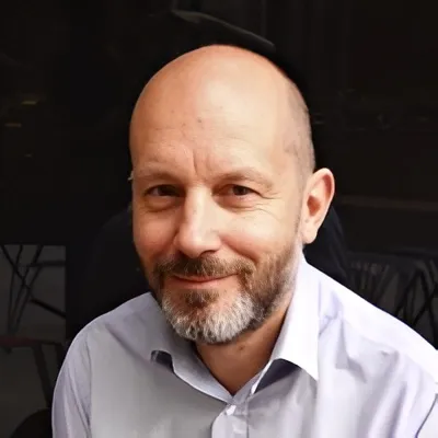 Professional man with a beard smiling, wearing a light blue shirt, representing financial expertise and client-focused service in a corporate setting.