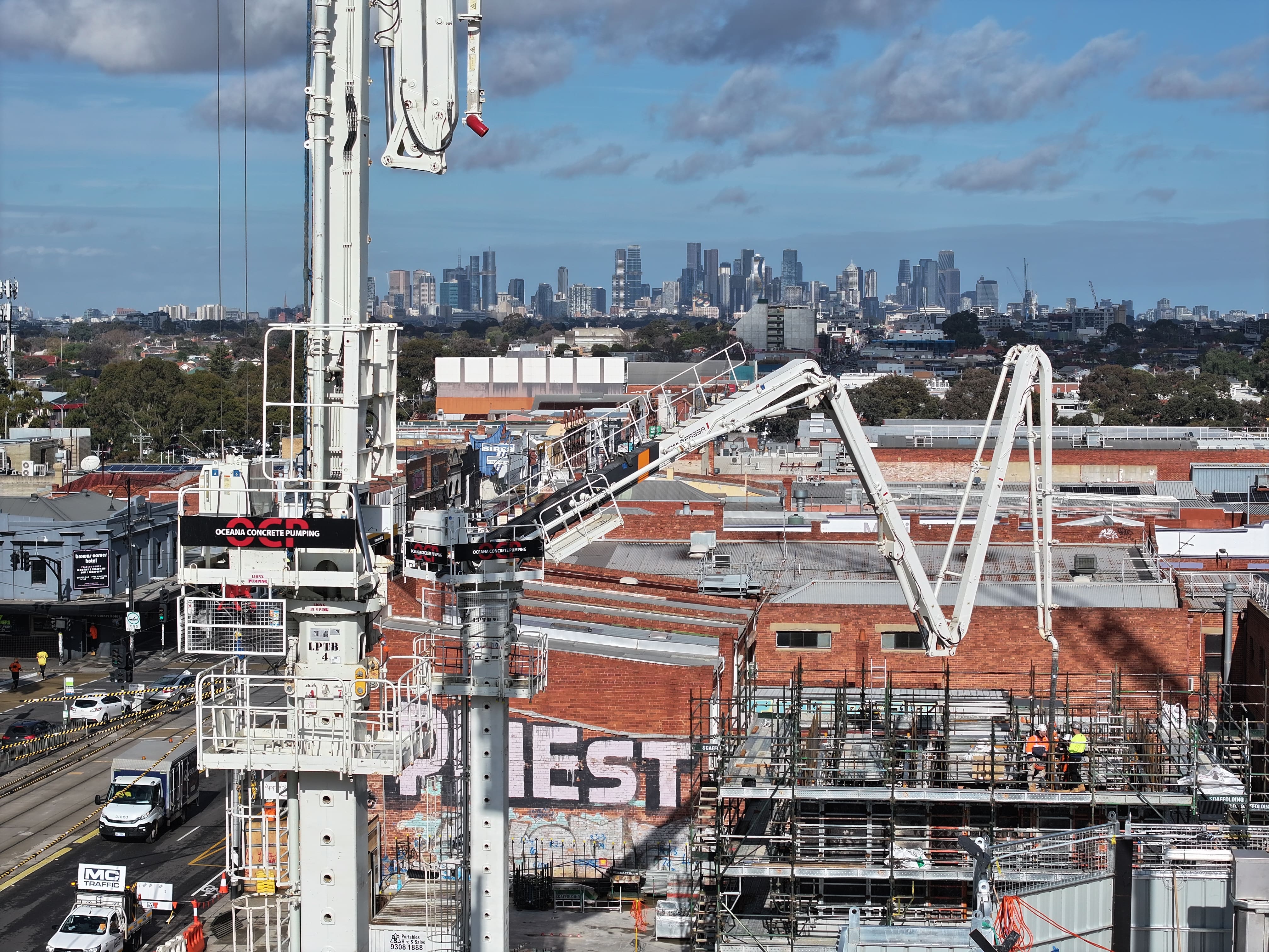 Oceana Concrete Pumping tower boom pump operating on a construction site in Melbourne with city skyline in the background.